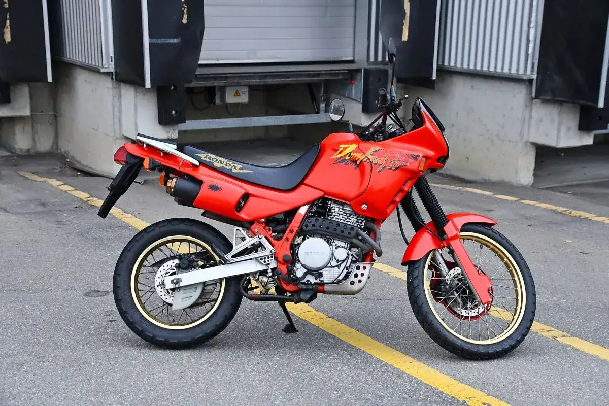 Czerwony motocykl Honda Dominator z lat 90. stoi na asfalcie, gotowy na przygodę.