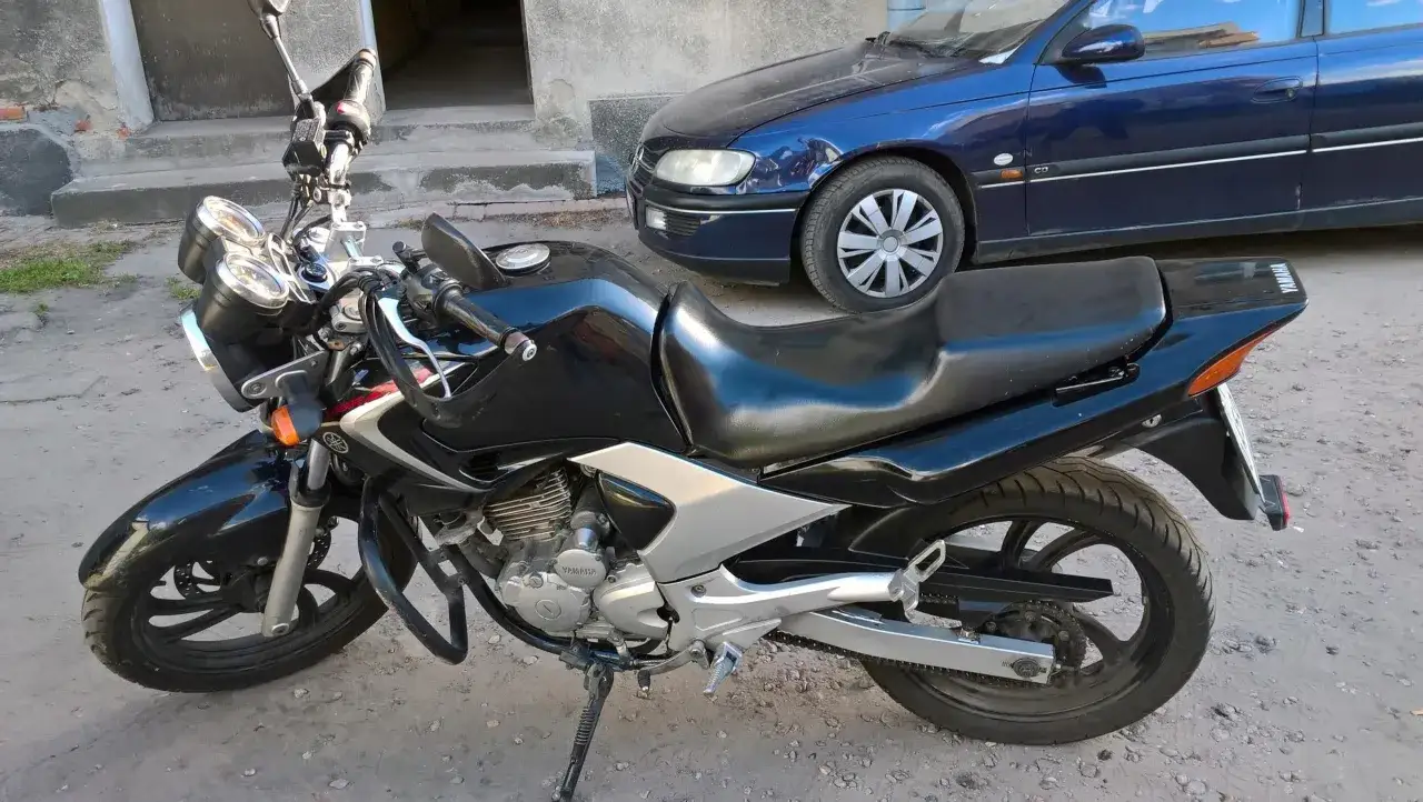 Czarny motocykl Yamaha YBR 250 z chromowanymi elementami, zaparkowany obok niebieskiego samochodu.