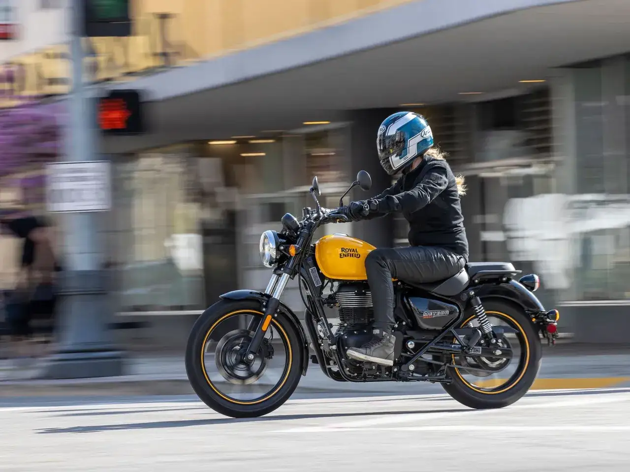 Kobieta w kasku jedzie żółtym motocyklem Royal Enfield Meteor 350 przez miasto.