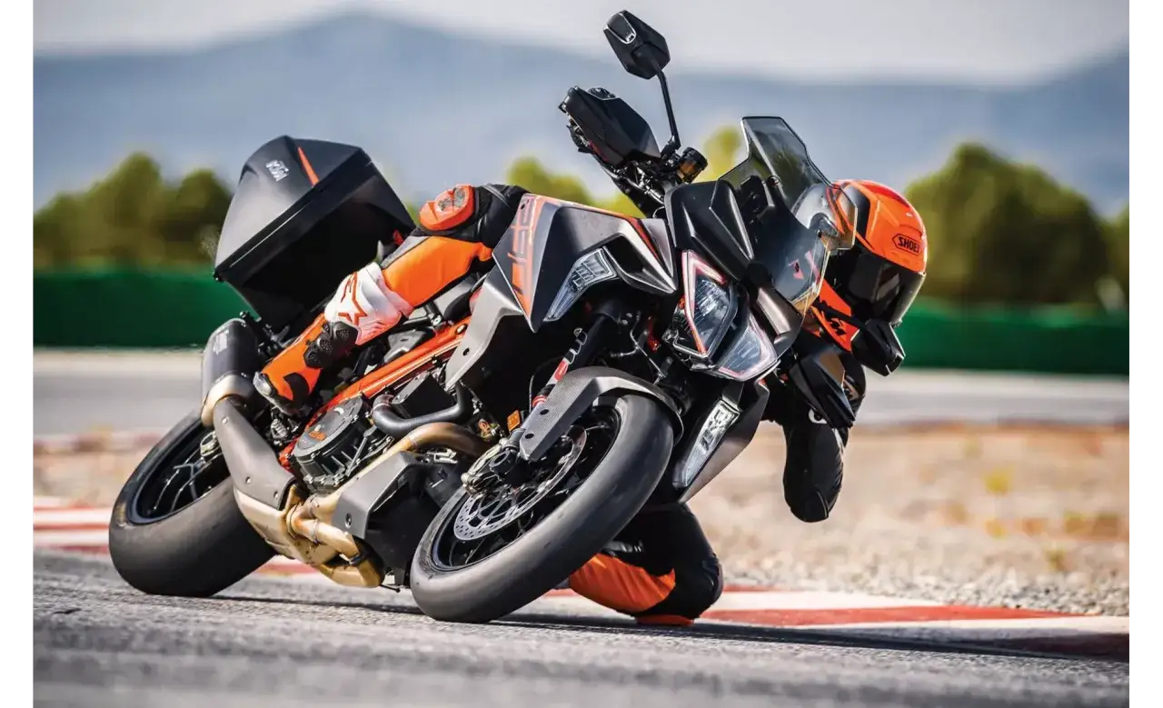 Motocyklista w pomarańczowym kombinezonie pochyla się na torze wyścigowym na swoim KTM 1290 Super Duke.