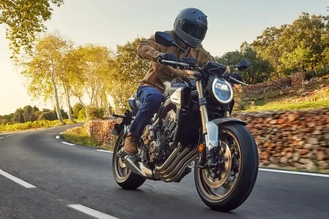 Motocyklista w kasku pędzi na swoim Honda cb650r po malowniczej drodze wśród drzew i kamiennych murków.