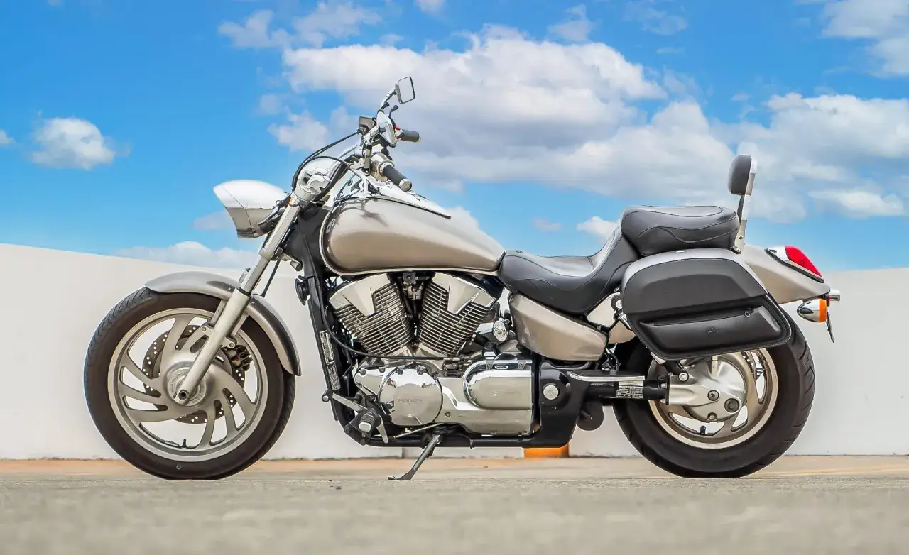 Srebrny motocykl Honda VTX 1300 z sakwami, gotowy na podróż pod błękitnym niebem z chmurami.