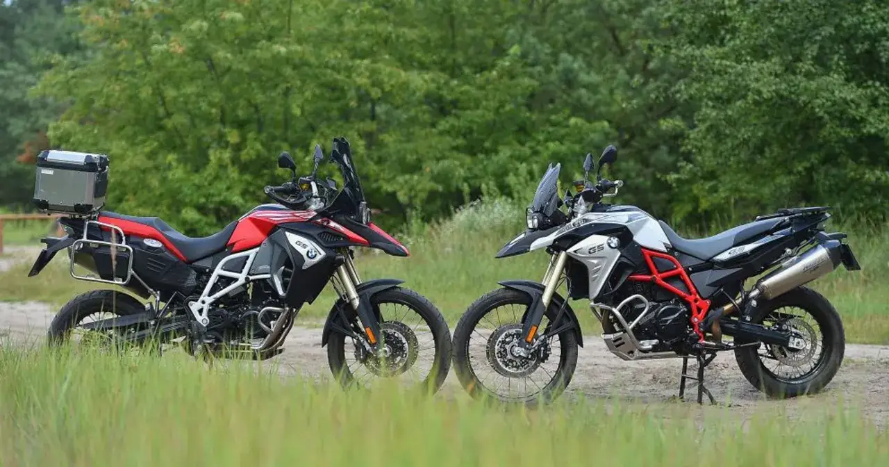 Dwa motocykle BMW 800 GS, jeden czerwony, drugi srebrny, stoją na tle zieleni.