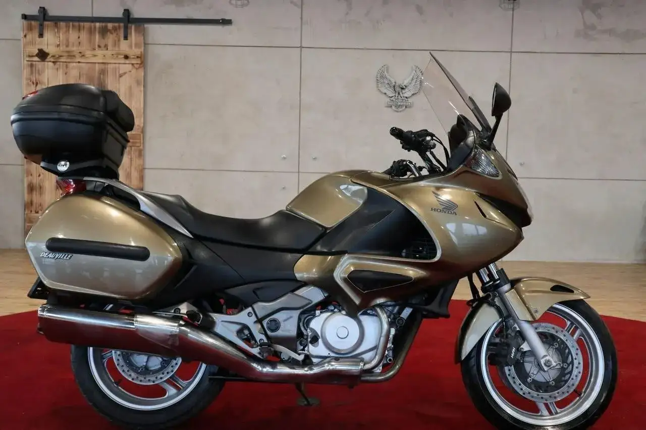 Złoty motocykl Honda Deauville z kufrem i sakwami, gotowy na dalekie podróże.