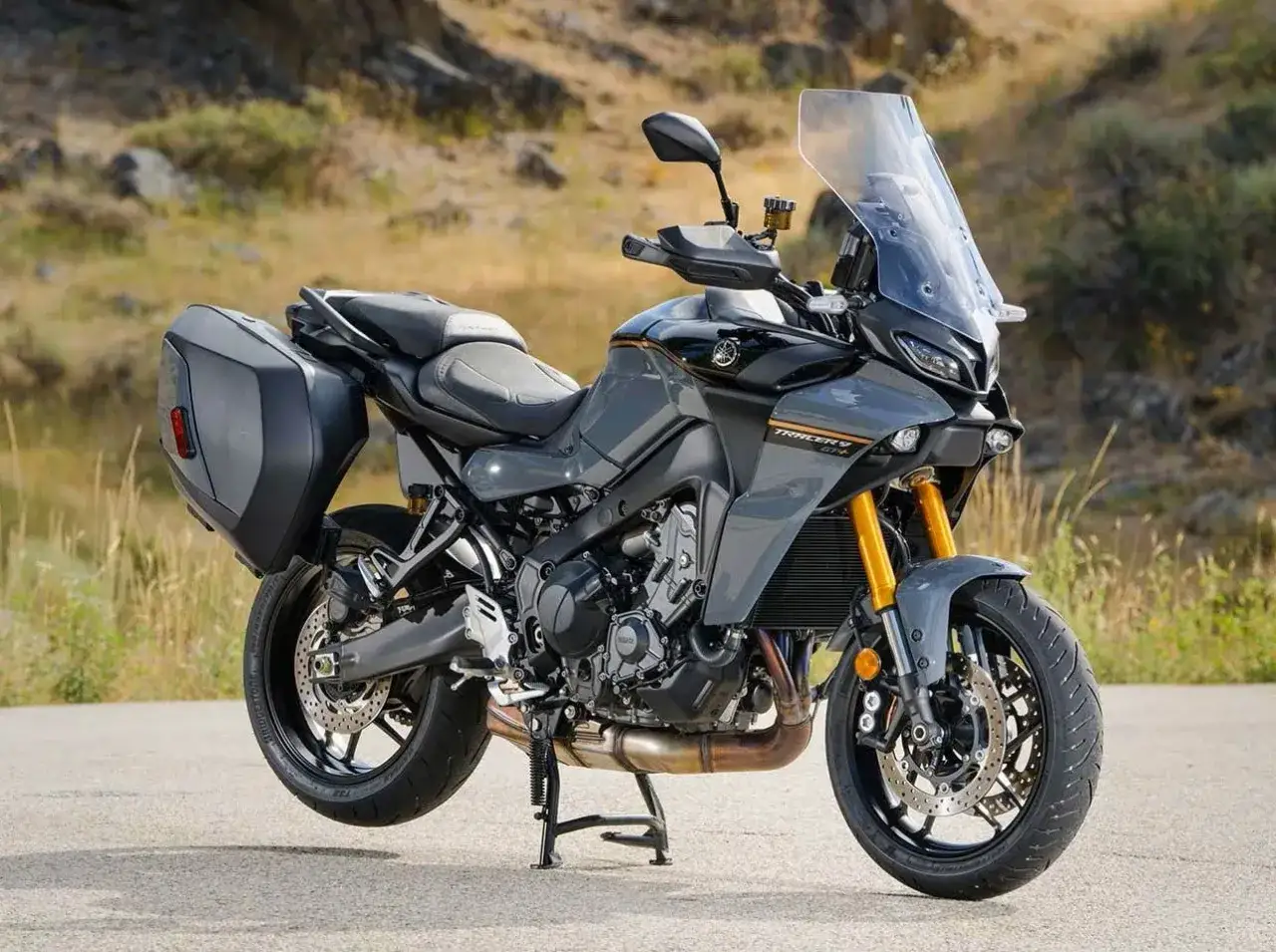 Szary motocykl szosowo turystyczny Yamaha Tracer 9 GT z kuframi, gotowy na dalekie podróże po krętych drogach.