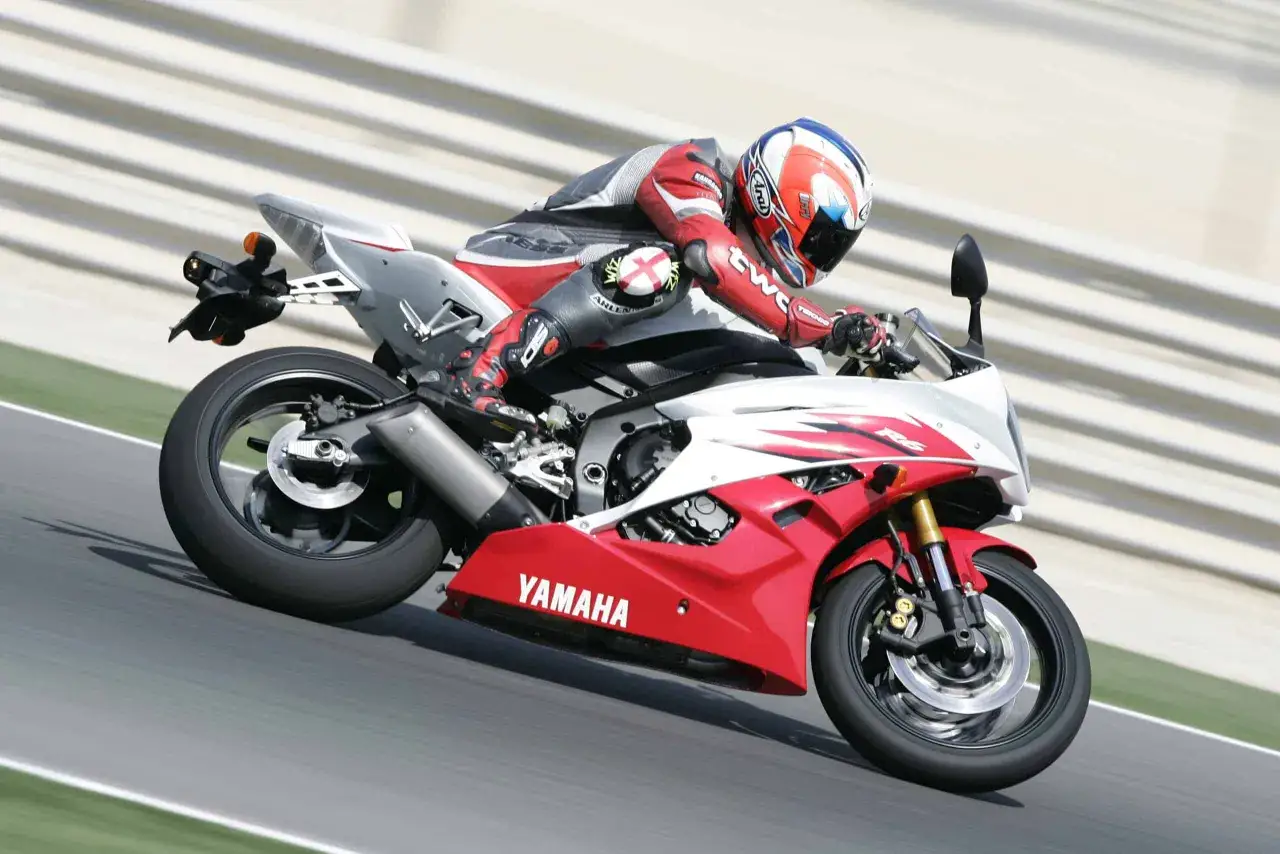 Motocyklista w czerwonym kombinezonie wykonuje ostrą jazdę motocyklem 600 na kat B. Yamaha R6 na torze wyścigowym.