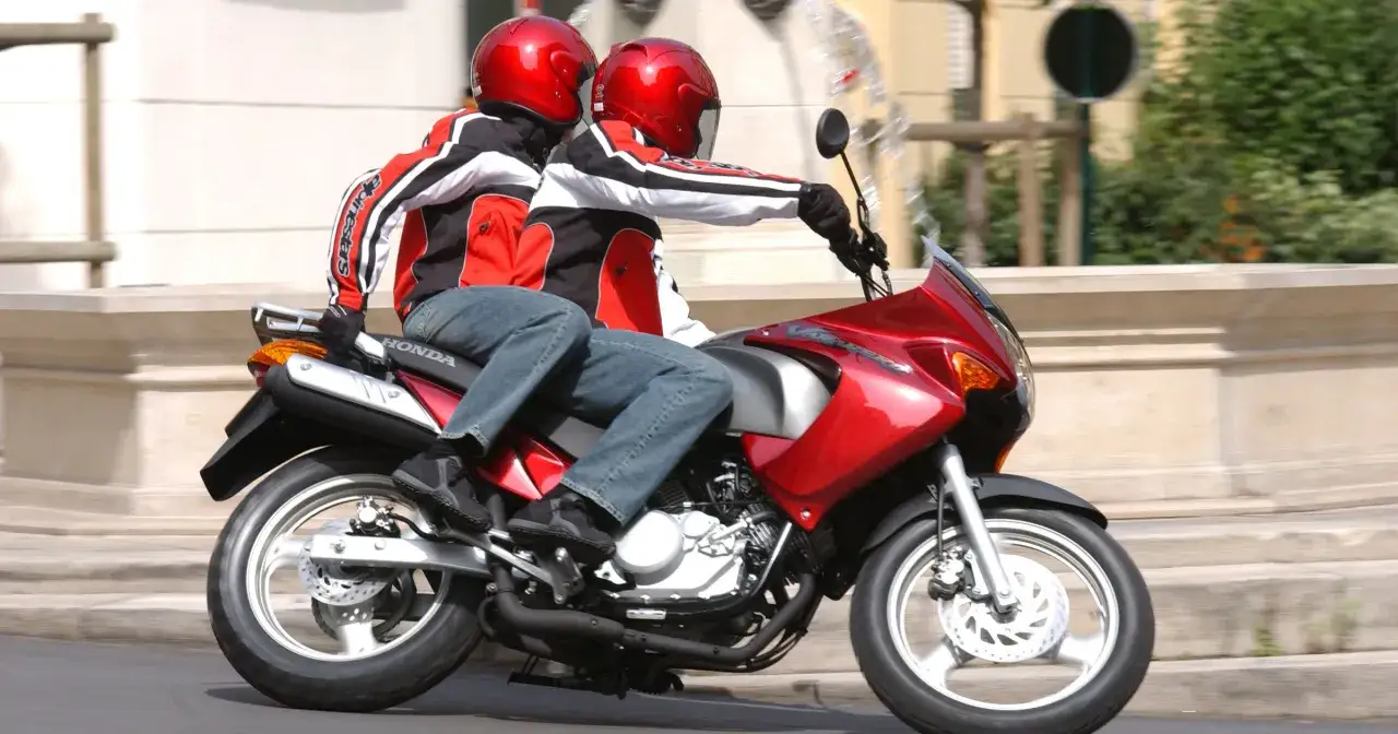 Dwie osoby w czerwonych kaskach i kurtkach jadą na czerwonym motocyklu Honda. To ich pierwsza jazda 125 na bezdrożach, ale czują się pewnie.