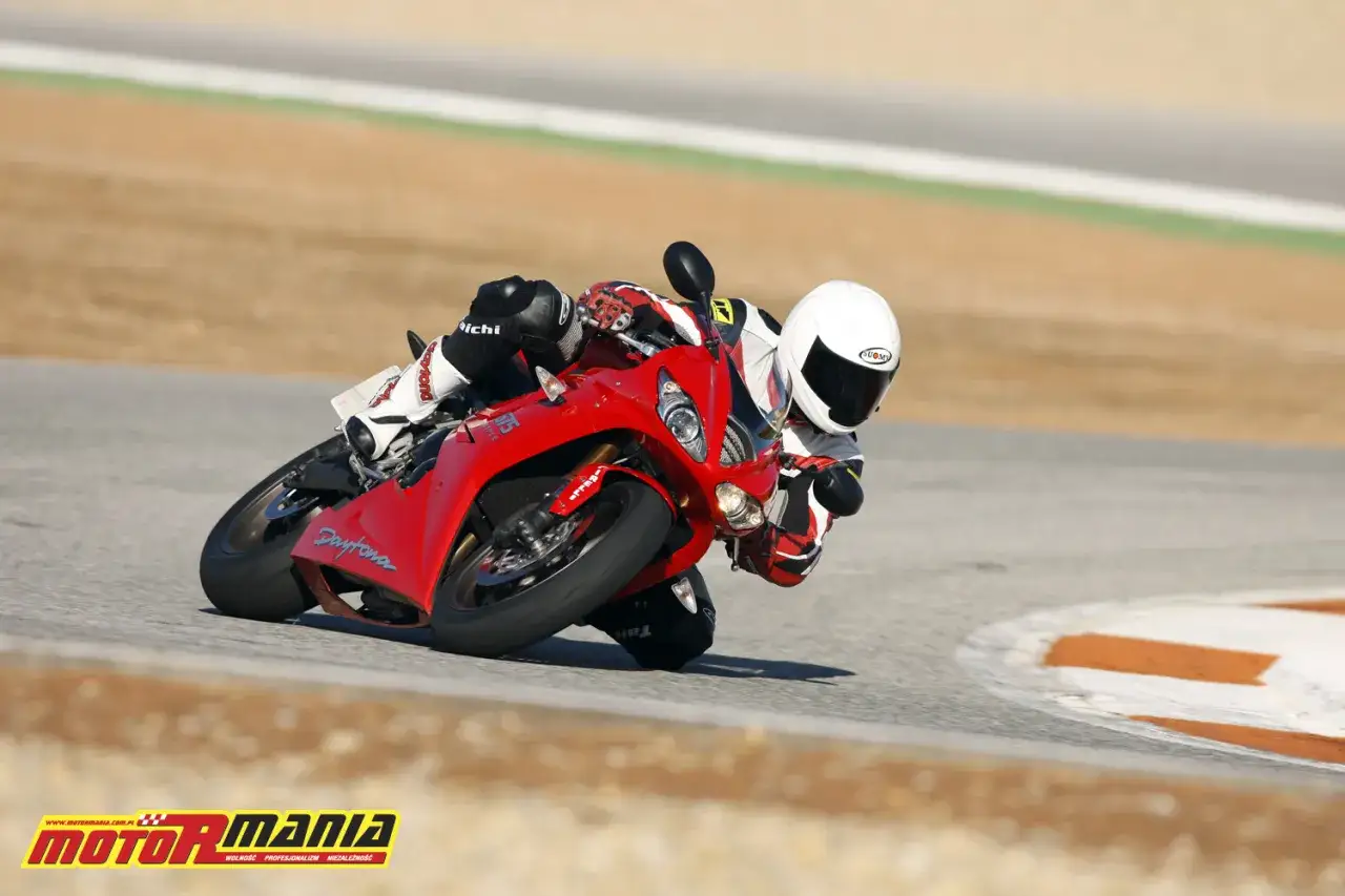 Motocyklista w czerwonym stroju wykonuje ostry zakręt, pochylając się mocno na torze. Jego technika jazdy, zwana przeciwskrętem, pozwala na szybkie pokonywanie zakrętów.