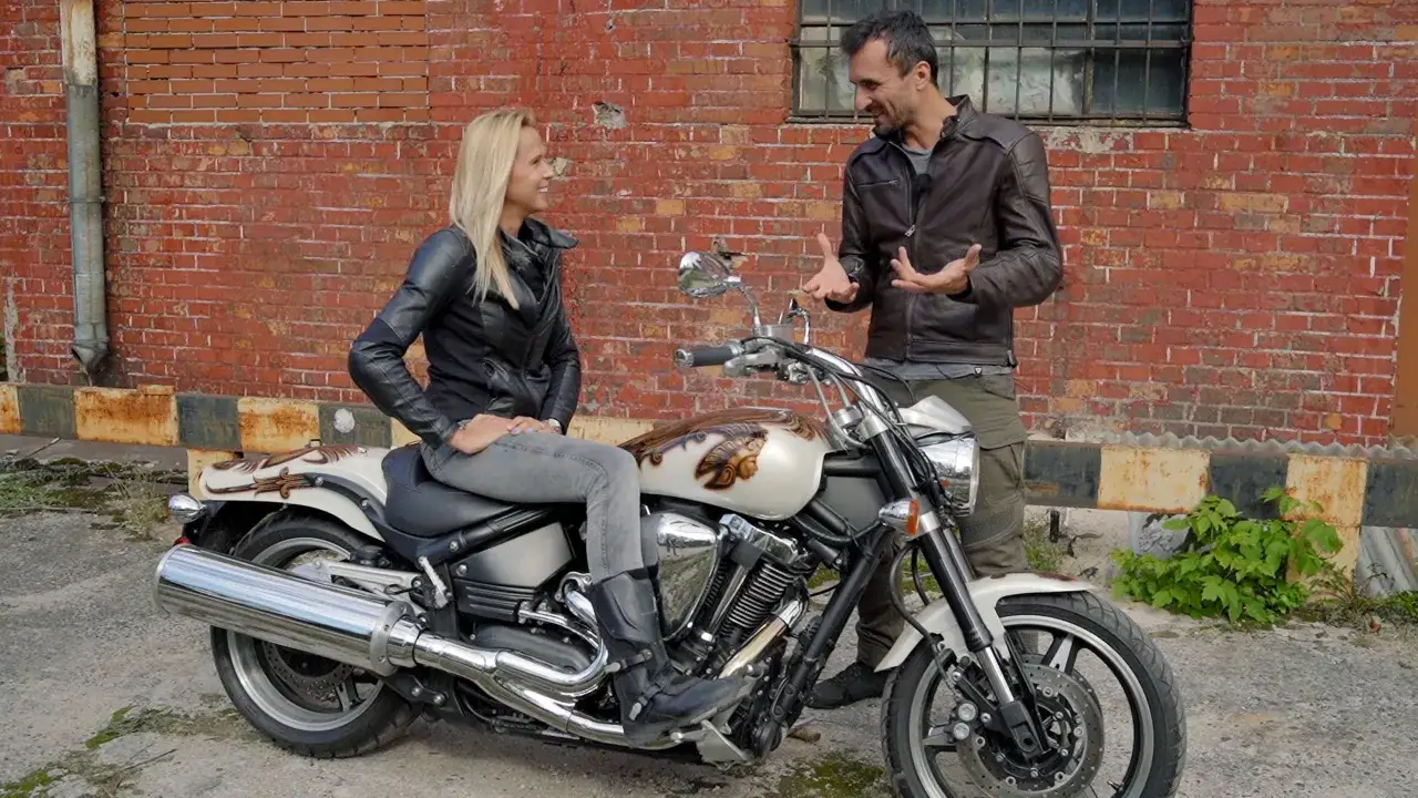 Kobieta siedzi na motocyklu Yamaha Warrior 1700, mężczyzna stoi obok, rozmawiając.
