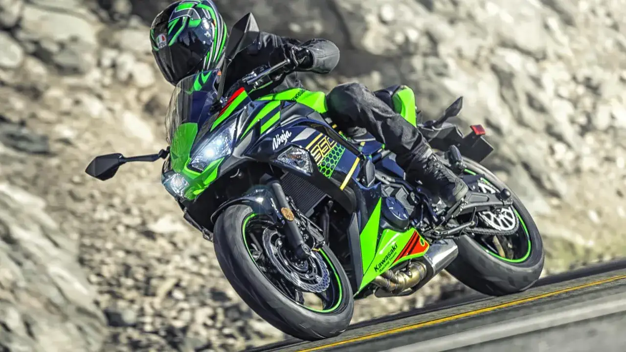Motocyklista na zielono-czarnym Kawasaki Ninja 650, z widocznymi danymi technicznymi na owiewce, pokonuje zakręt na górskiej drodze.