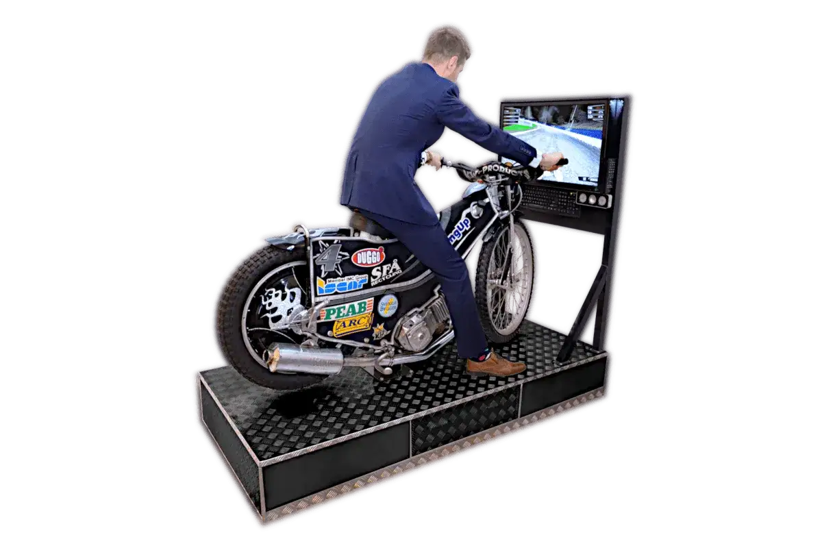 Mężczyzna w garniturze siedzi na motocyklu żużlowym, grając w symulator wyścigów.