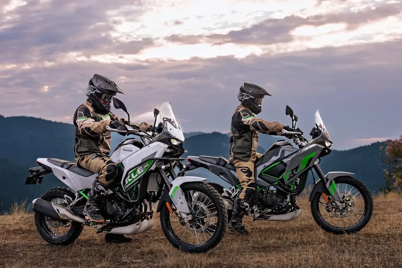 Dwóch motocyklistów na motocyklach Kawasaki KLR. Jeden biały, drugi szary z zielonymi akcentami, gotowi na przygodę w górach.