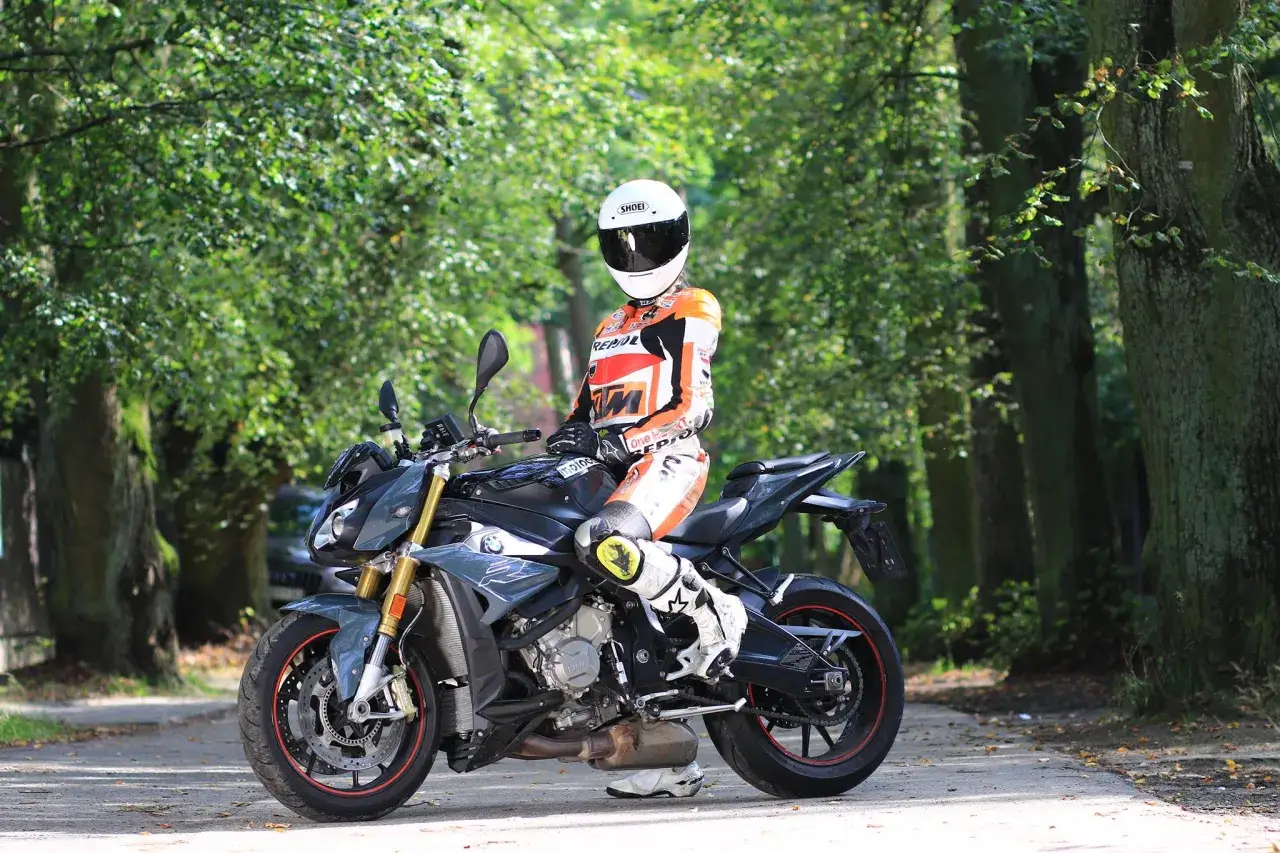 Motocyklista w kombinezonie siedzi na sportowym motocyklu BMW S1000R wśród zieleni.