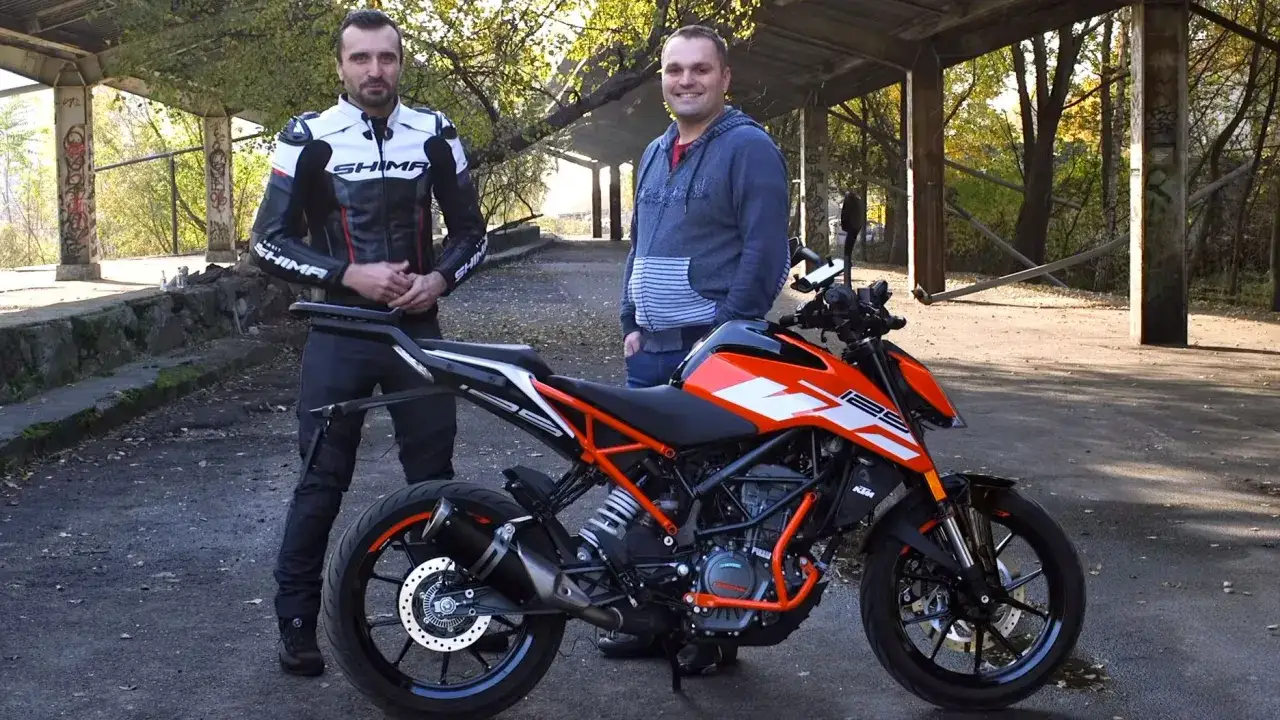 Dwóch mężczyzn obok pomarańczowo-czarnego motocykla KTM Duke 125. Sprawdzamy jego dane techniczne.