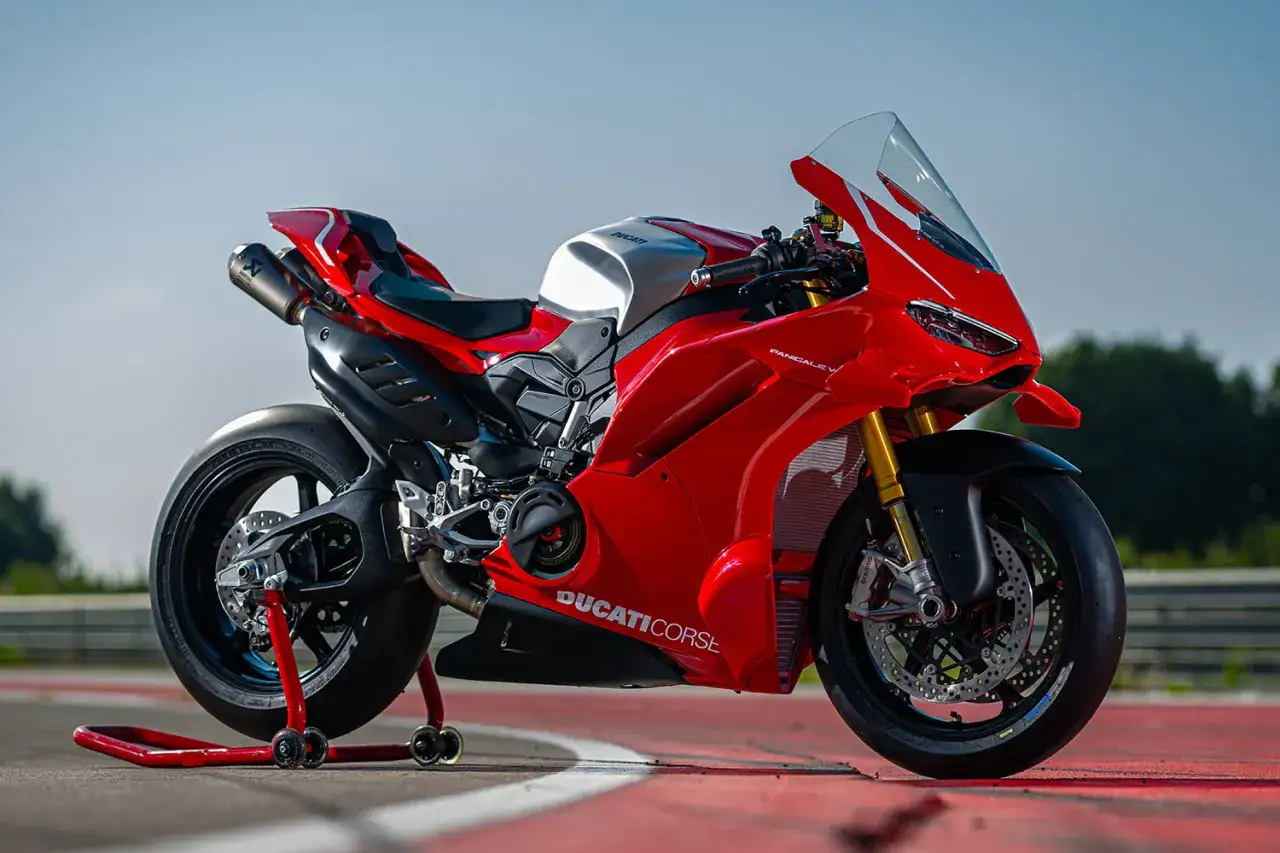 Czerwony motocykl Ducati Panigale V4 na czerwonym tle toru wyścigowego, gotowy do jazdy.