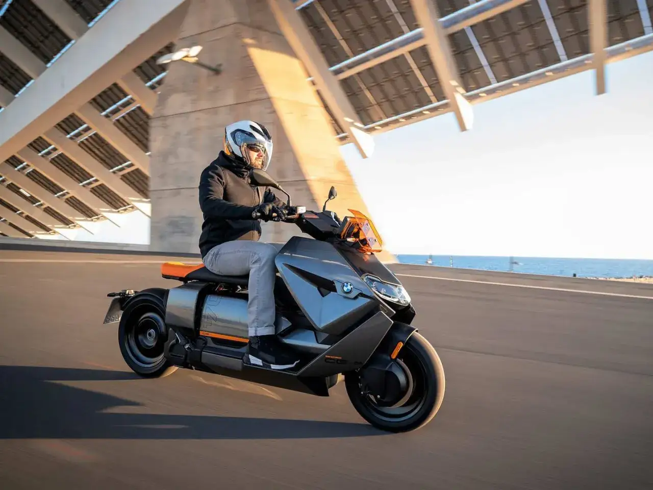 Mężczyzna w kasku jedzie na futurystycznym skuterze BMW CE 04 wzdłuż wybrzeża.