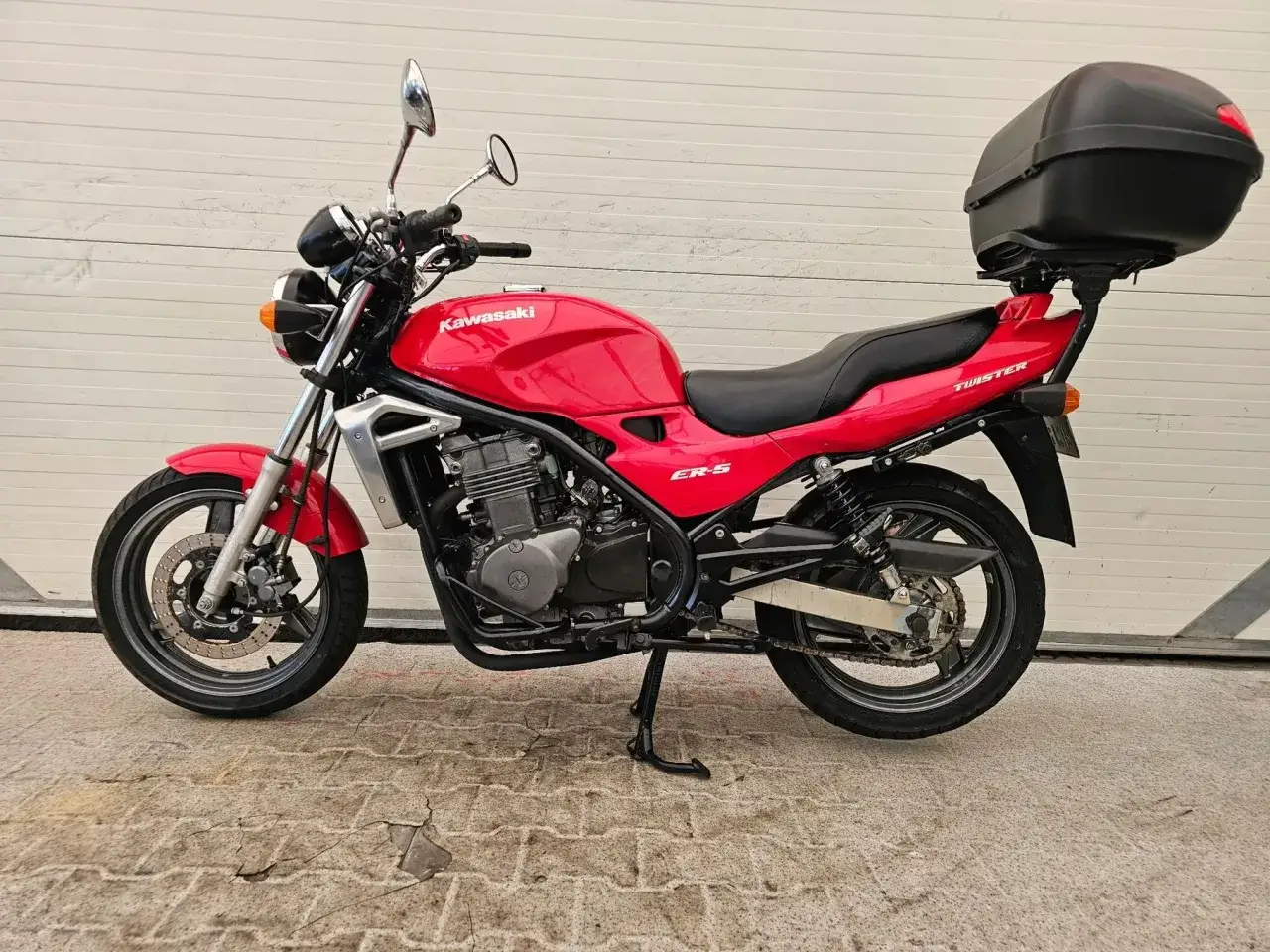 Czerwony motocykl Kawasaki ER-5 z czarnym kufrem na bagażnik, gotowy na podróż.