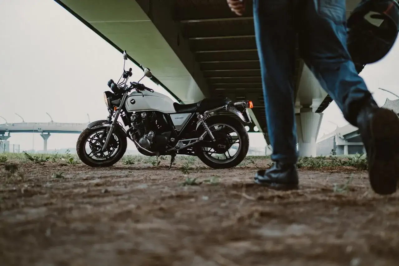 Biały motocykl na A2, zaparkowany pod estakadą. Obok przechadza się motocyklista z kaskiem w dłoni.
