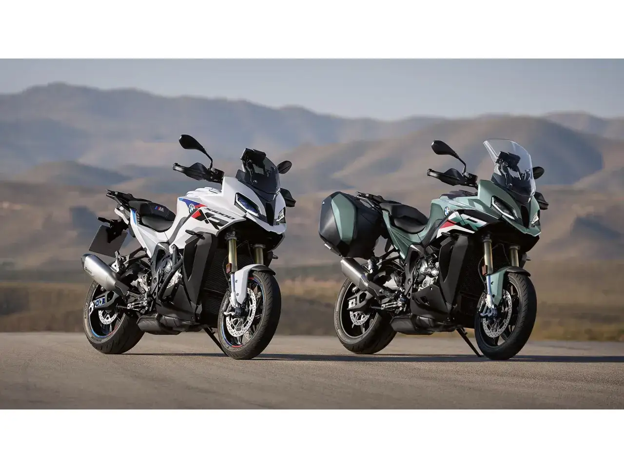 Dwa motocykle BMW XR w różnych kolorach, biały i zielony, stojące na drodze z górami w tle.