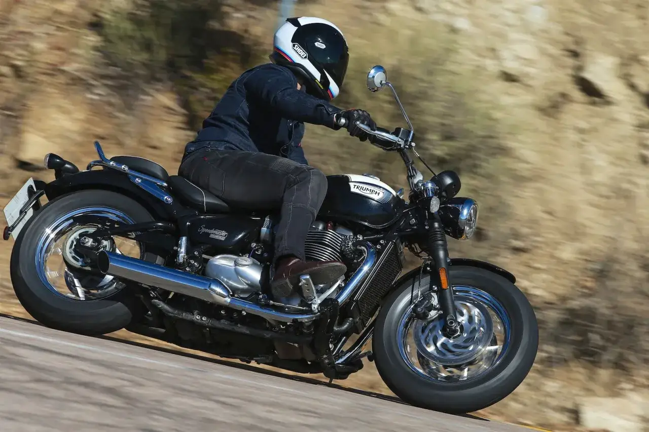 Motocyklista w kasku jedzie na czarnym Triumph Speedmaster po krętej drodze.