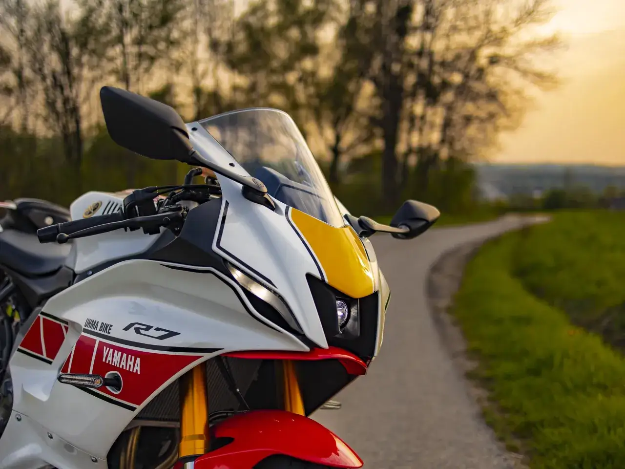 Sportowy motocykl Yamaha R7 z czerwono-biało-żółtymi akcentami na tle drogi i drzew. Dane techniczne tego modelu są imponujące.