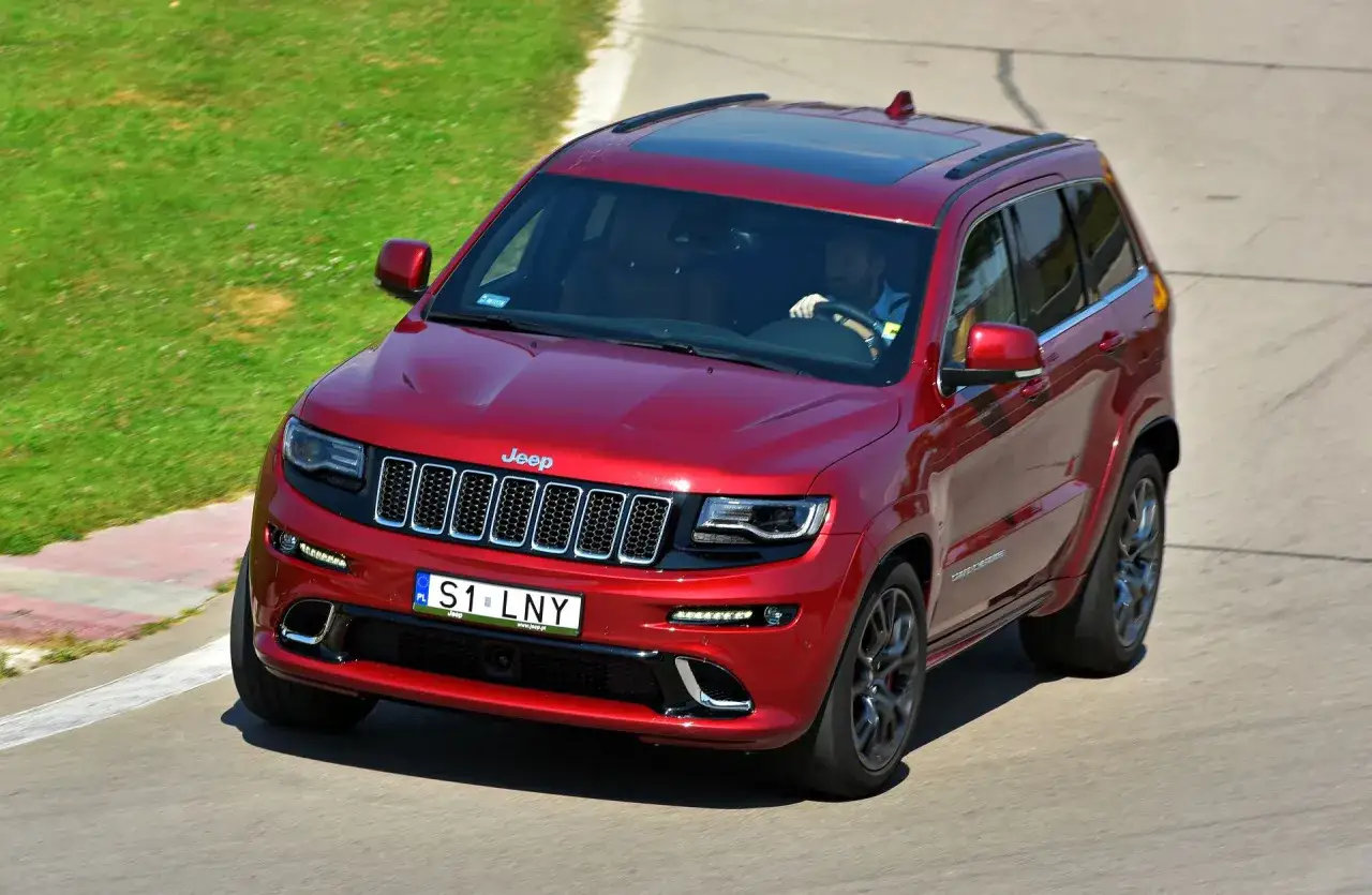 Czerwony Jeep Grand Cherokee na torze wyścigowym, kierowca z tablicą rejestracyjną S1 LNY. To jego indywidualna rejestracja.