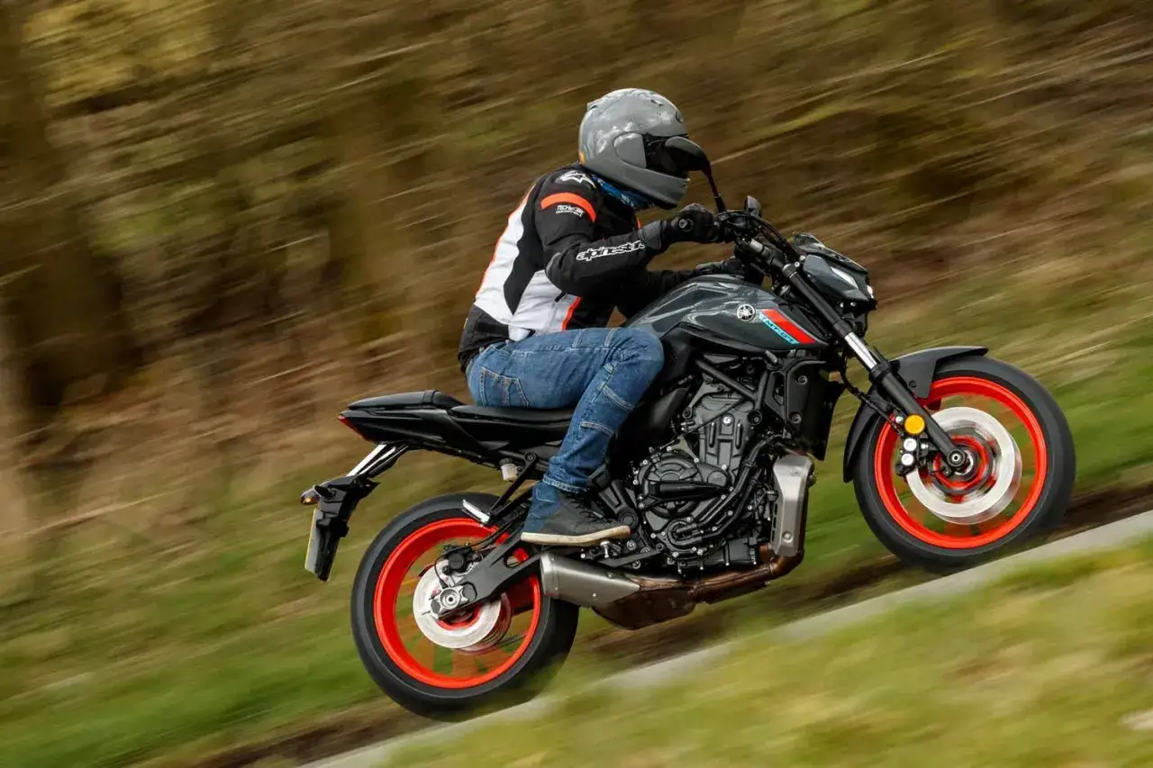Motocyklista na szarym Yamaha MT-07 z czerwonymi felgami pokonuje zakręt. Niska waga tego modelu ułatwia manewrowanie.