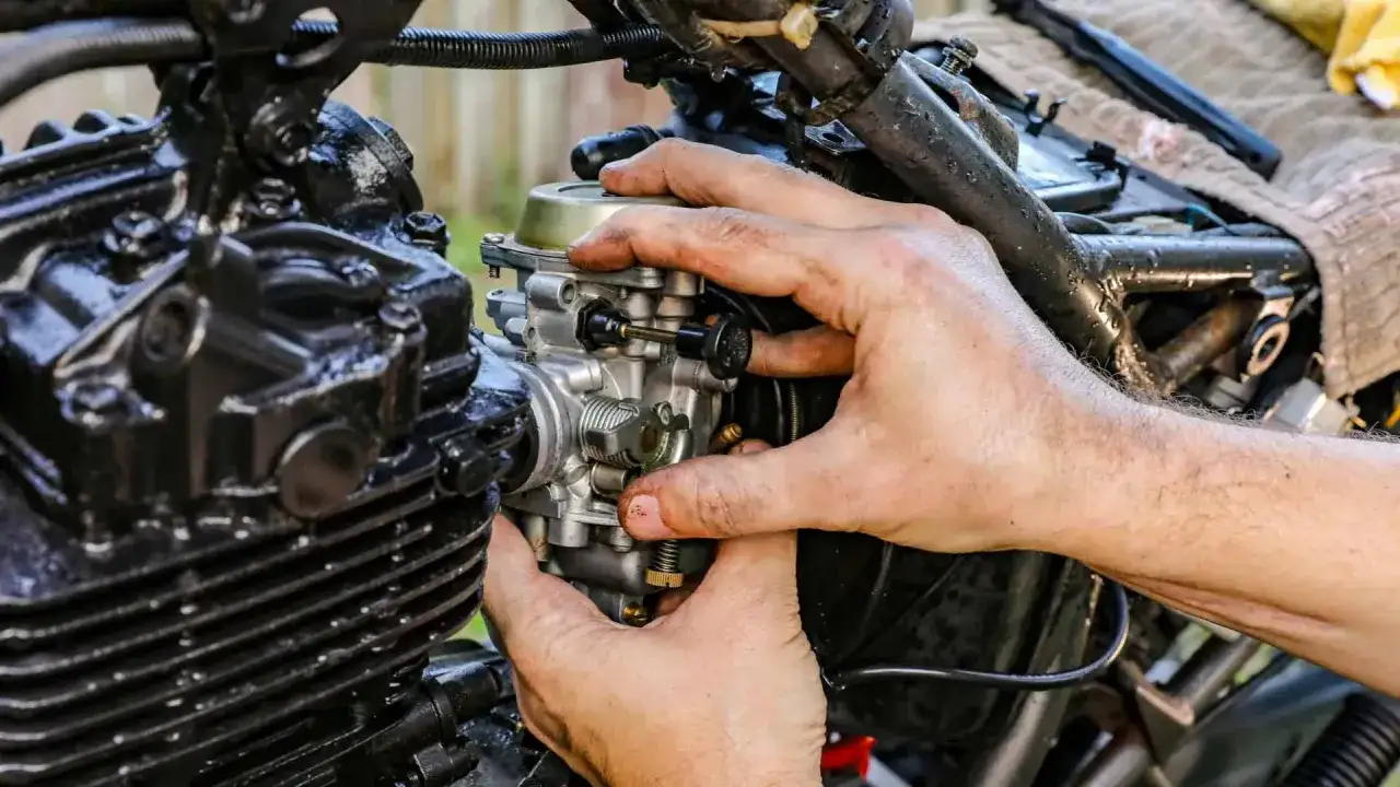 Dłonie majsterkowicza regulują gaźnik motocykla, kluczowy element odpowiedzialny za symbol ssania paliwa.