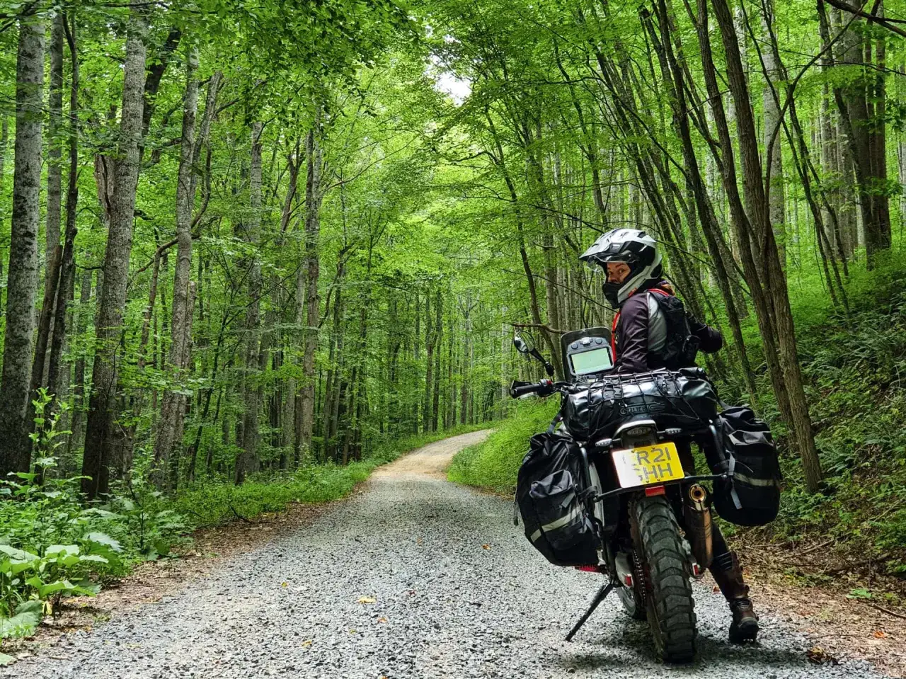 Motocyklista w kasku na drodze szutrowej wśród bujnej zieleni lasu.