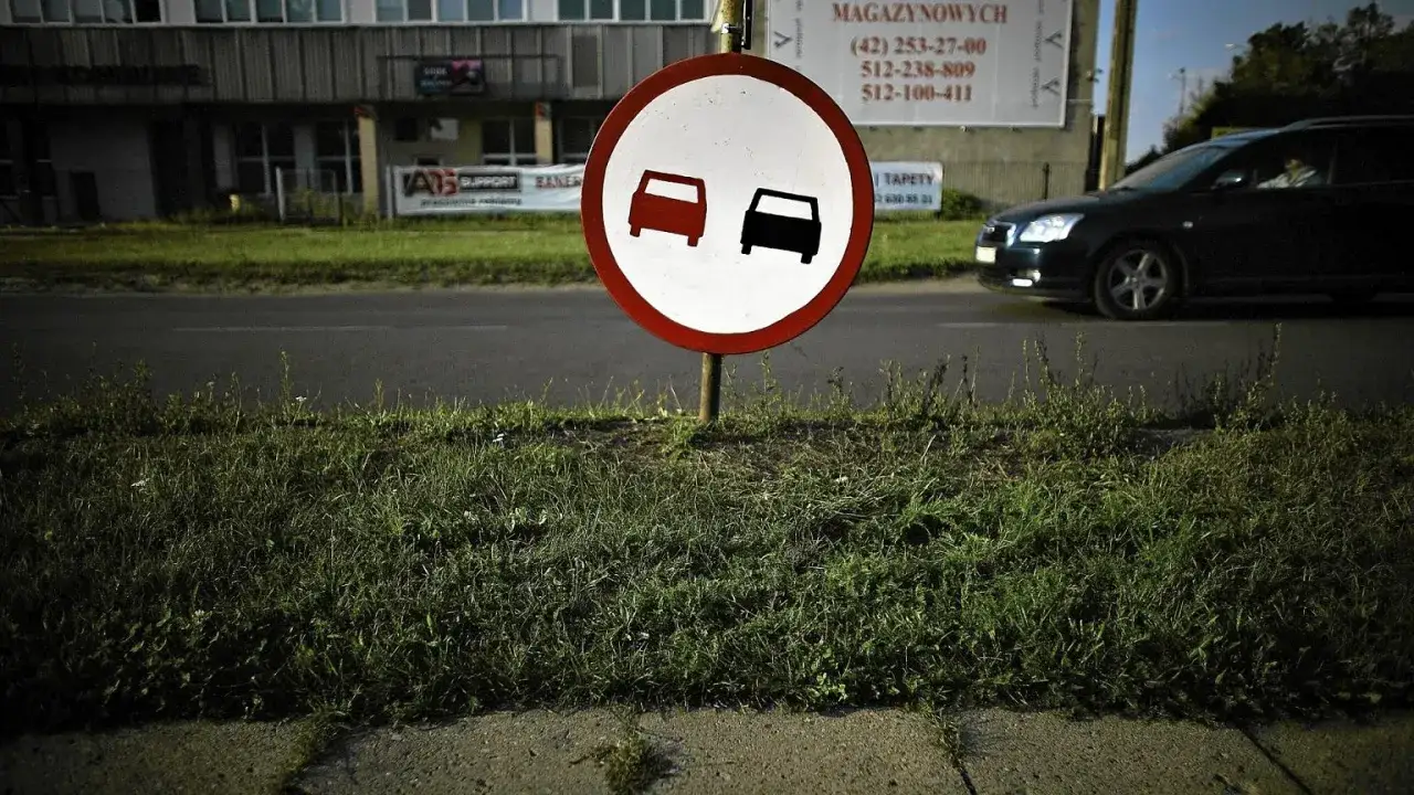 Znak zakazu wyprzedzania. Dwa samochody, jeden czerwony, drugi czarny, symbolizują zakaz wymijania i omijania.
