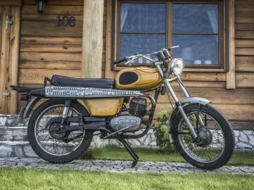 Żółty motorower WSK 175, z widocznymi danymi technicznymi na silniku, stoi przed drewnianym domem.